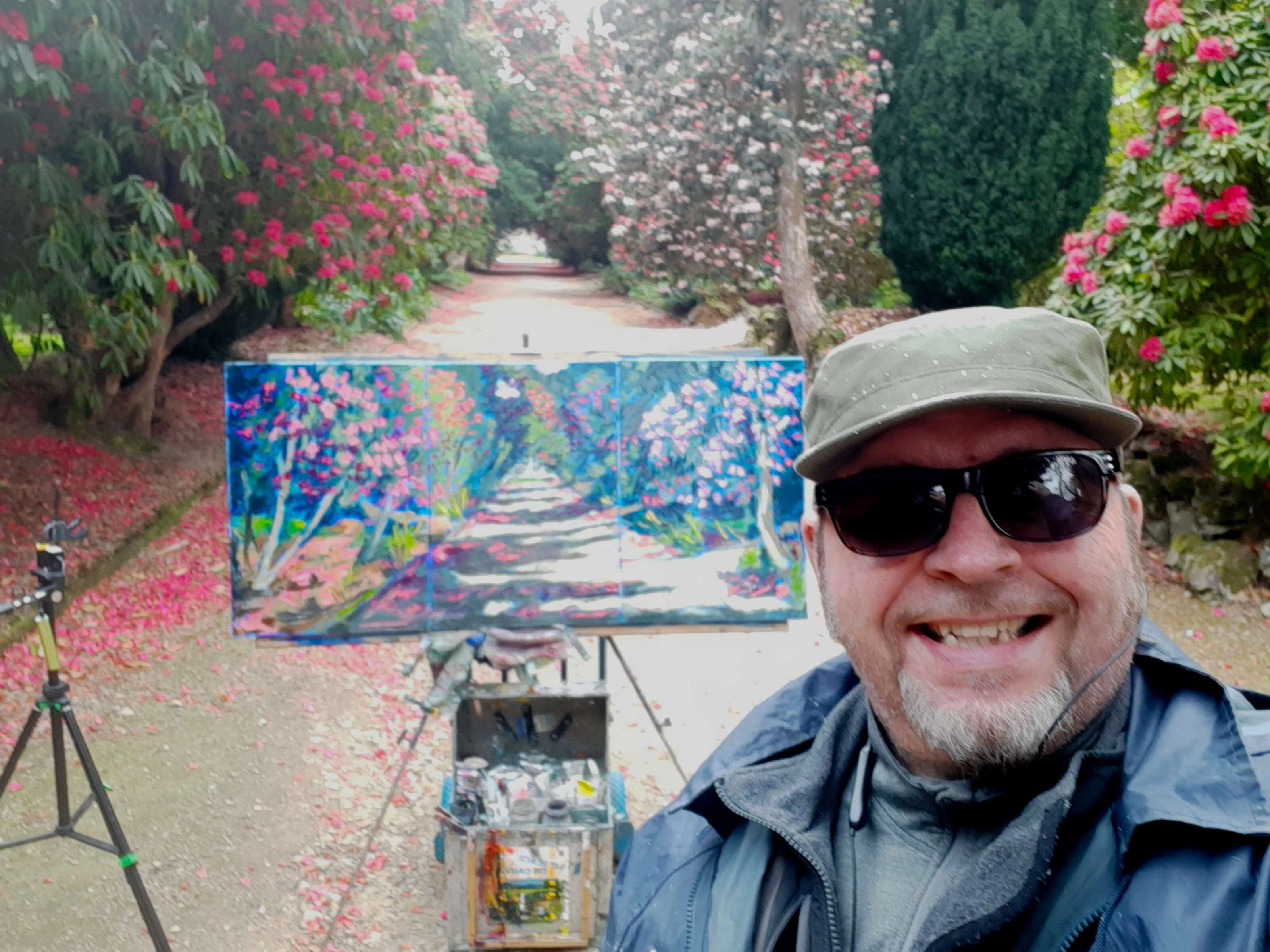 rod coyne does a piece to camera at the end of his latest plein air painting video. the canvas and subject matter are visible over his shoulder.